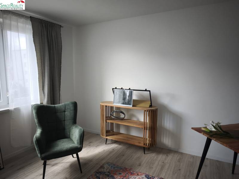 A room in a two-room apartment with an armchair, a table, and a floor with a wooden decor.