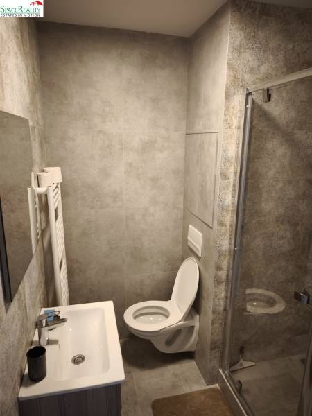 Bathroom in a 2-room apartment with a shower, sink, and toilet, gray tiles.