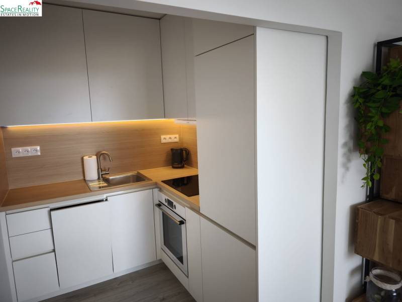 A kitchen in a 2-room apartment with light cabinets and a wooden decor floor.