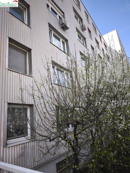 The exterior of an apartment building on Mozartova Street, Bratislava - Staré Mesto, surrounded by blooming trees.