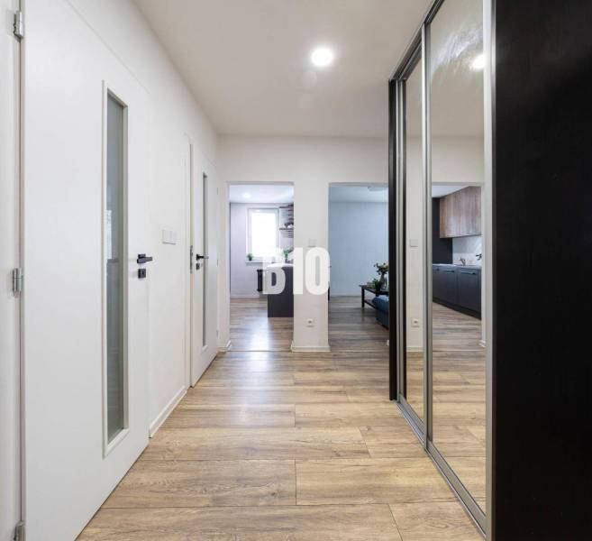 A hallway with a wooden decor floor, white doors, and built-in wardrobes in a 3-room apartment.