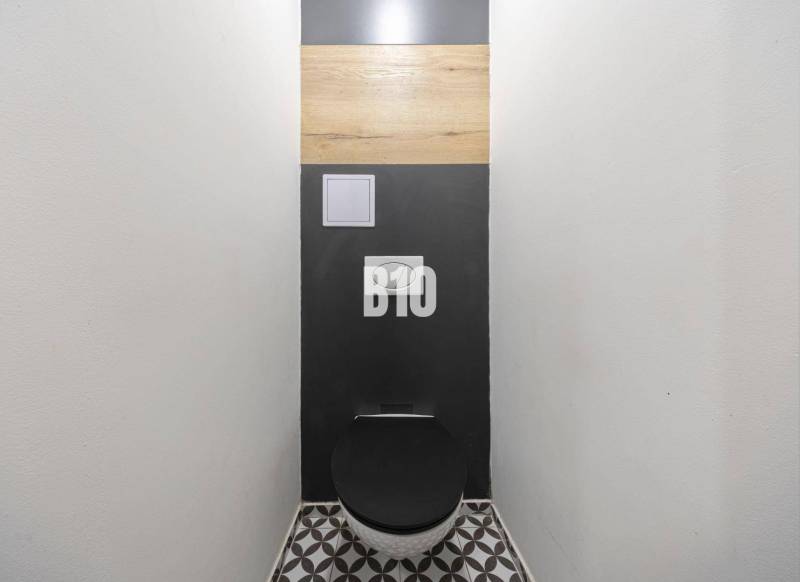 A toilet with a black seat and a geometric floor in a 3-room apartment.