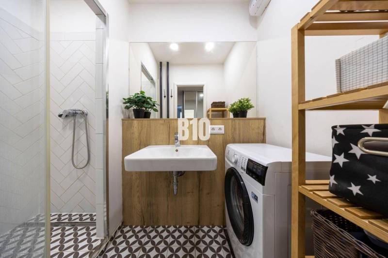The bathroom in the 3-room apartment includes a shower, a sink, a washing machine, and a wooden shelf.