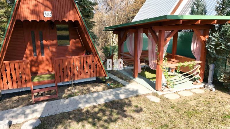 A wooden cottage in Martin next to a gazebo with pink curtains on a grassy area.