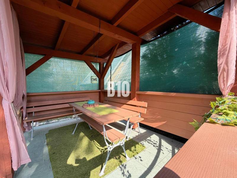 A wooden gazebo by the cottage in Martin with benches and a table, protected by a screen.