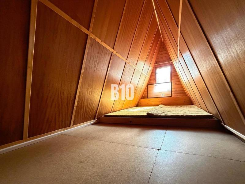 Attic of a cottage with a mattress and a window, wooden interior.