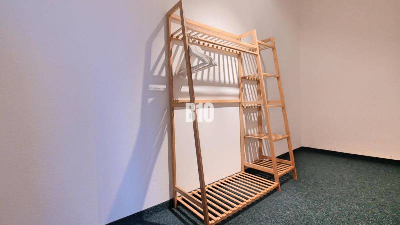 A wooden stand with hangers in a 3-room apartment on a dark carpet.