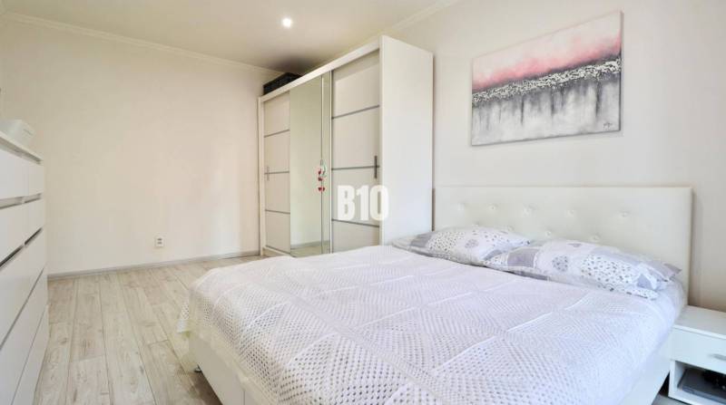A bright bedroom with a double bed, a built-in wardrobe, and a wooden decor floor in a 2-room apartment.
