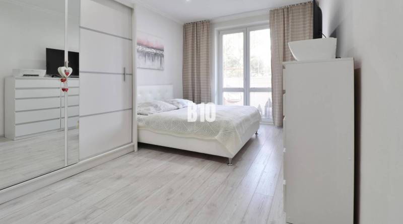 A bright bedroom with a large bed, wardrobe, and wooden decor flooring in a 2-room apartment.