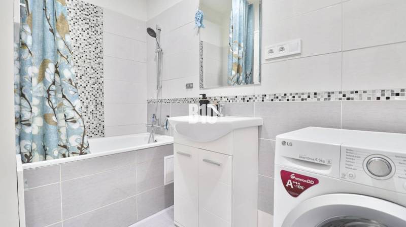 Bathroom in a 2-room apartment with a washing machine, a bathtub, and a floral-patterned curtain.