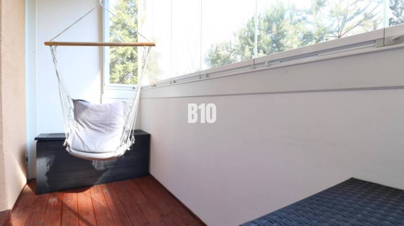 A glazed balcony in a 2-room apartment with a wooden decor floor and a hammock.