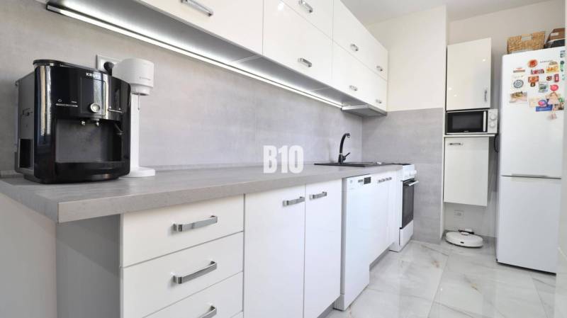 A kitchen in a 2-room apartment with white appliances and gray elements.