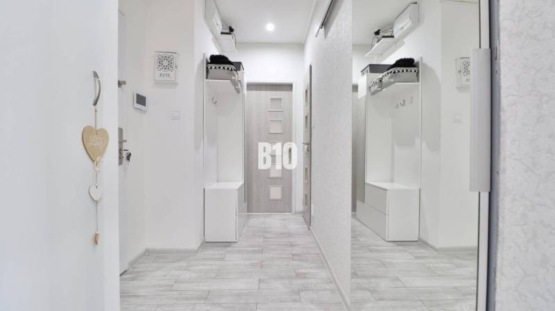 A hallway of a 2-room apartment with a coat rack wall and a wooden decor floor.