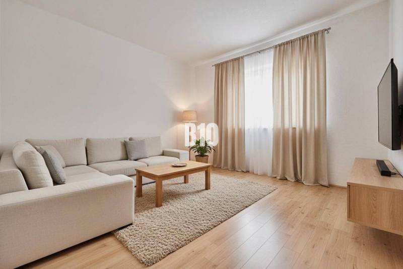 A living room of a family house with a beige sofa, a coffee table, and a wooden-patterned floor.