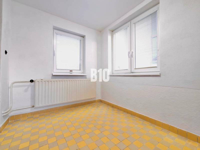 White wall, windows, radiator, and yellow tiled floor in a family house.