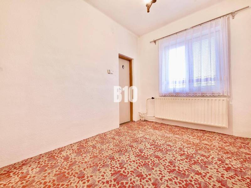 A room in a family house with a carpet, a radiator, and a curtain on the window.