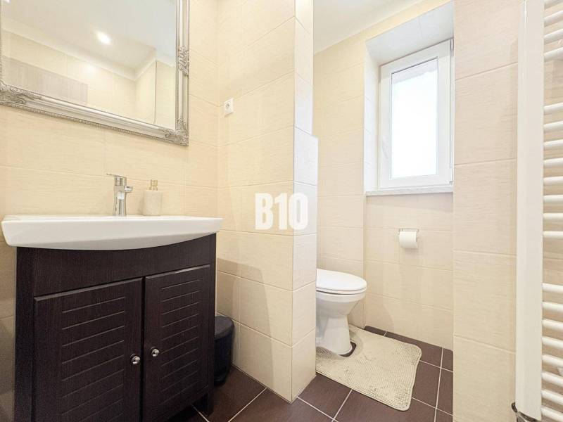 A bathroom in a 2-room apartment with a dark sink cabinet and a window.