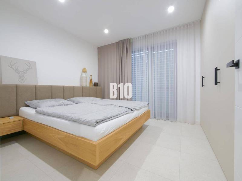 A bedroom in a family house with a double bed, light curtains, and a decorative painting.