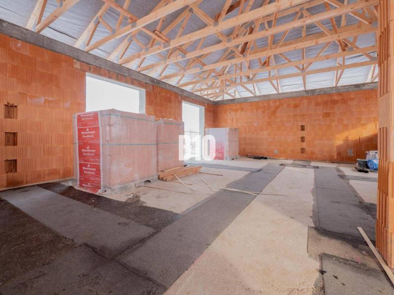 An unfinished interior of a family house with brick walls and a wooden ceiling frame.