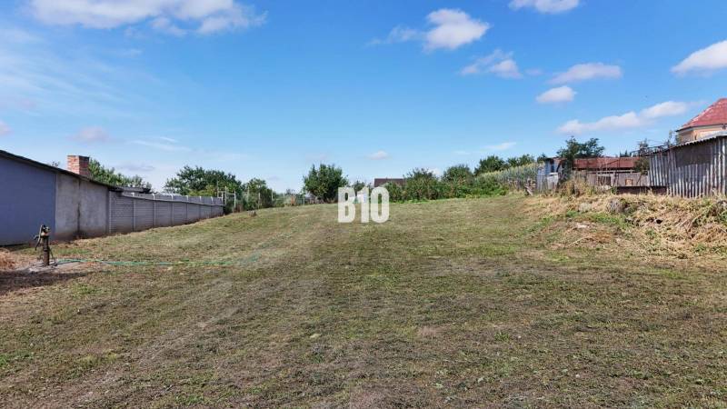A flat residential plot in Rumanová, surrounded by greenery and neighboring fences.