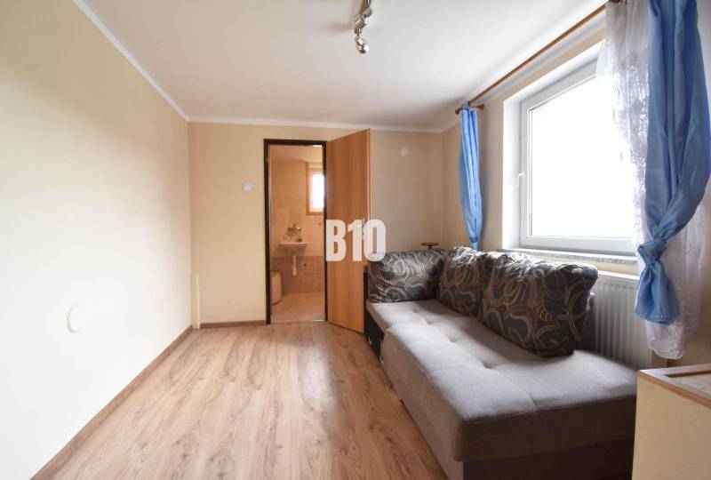 Living room in a family house with a sofa, a window with blue curtains, and a door to the bathroom.
