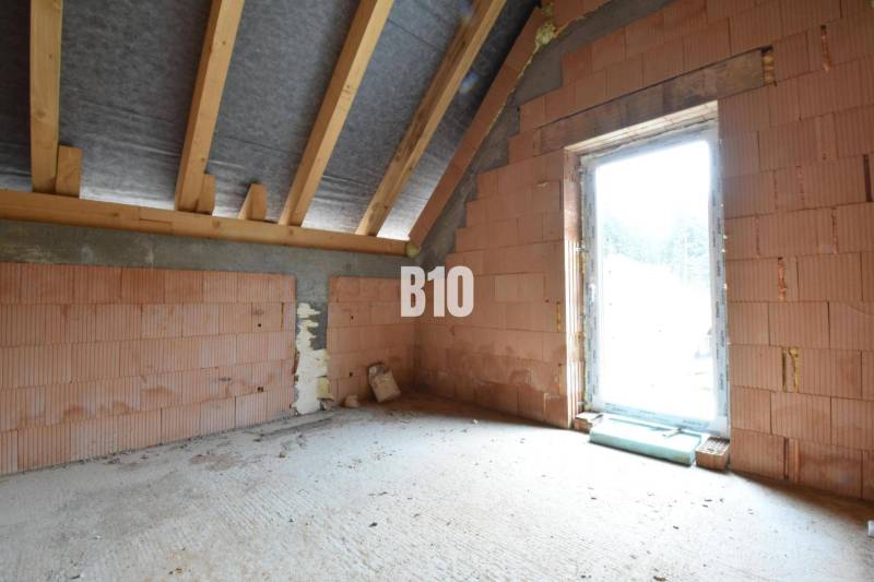 The ground floor of a family house showing raw brick walls and roof beams.