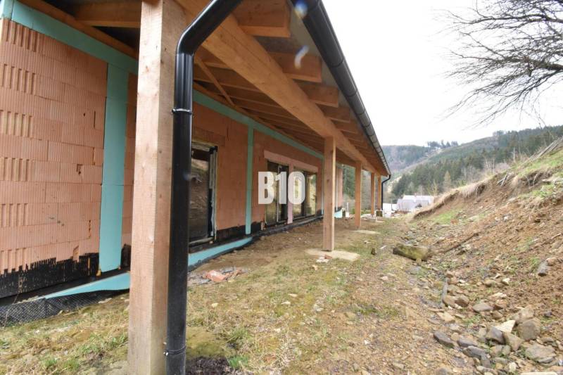 A family house under construction with a wooden shelter, flat terrain, and surrounding landscape.