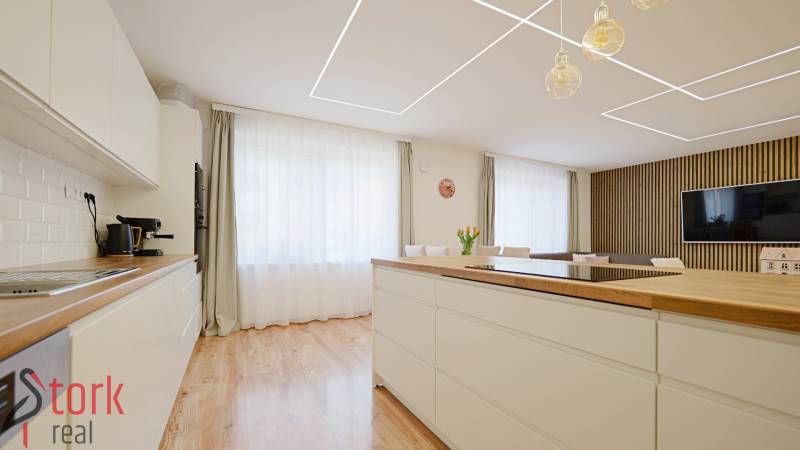 A kitchen in a family house with a wooden decor floor, light furniture, and a large window.
