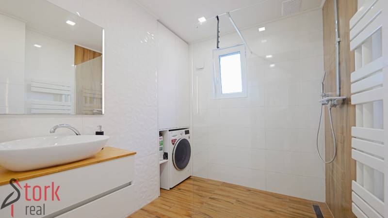 A bathroom with a washing machine, shower, sink, and a floor with a wooden decor in a family house.