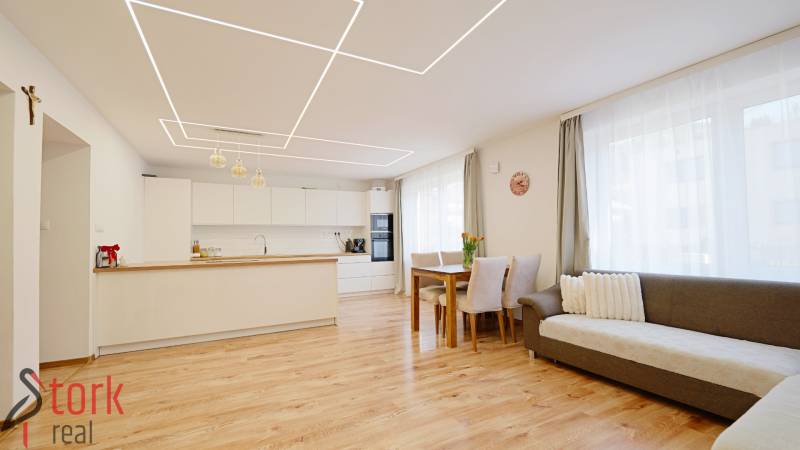 Interior of a family house with a kitchen and living room, wooden decor flooring, and light-colored furniture.