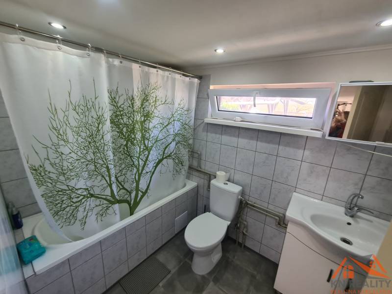 A bathroom in a cabin with tiles, a bathtub, and a curtain with a tree motif.