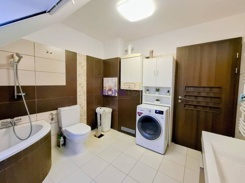 A bathroom in a 3-room apartment with a corner bathtub, a washing machine, and light tiles.