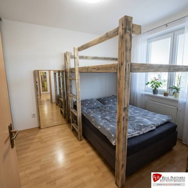 Bedroom in a 2-room apartment with a bunk bed, wooden decor flooring, and a mirror.