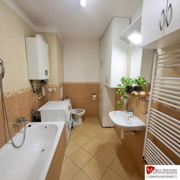 A bathroom with a bathtub, sink, and washing machine in a 2-room apartment with plants.