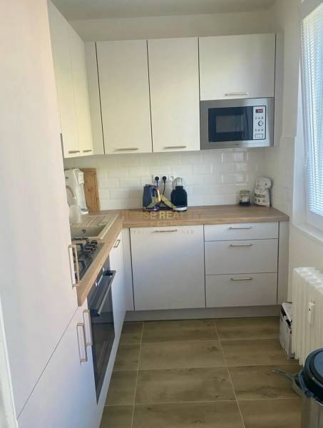 A kitchen in a 3-room apartment with white cabinets and a wood-patterned floor.