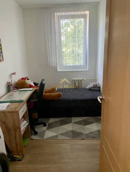 A small room in a 3-room apartment with a wooden decor floor, bed, table, chair.