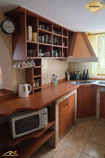 A kitchen in a family house with wooden cabinets and shelves, complemented by a wall clock.