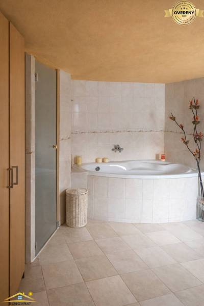 A bathroom in a family house with a corner bathtub, decorative flowers, and beige tiles.