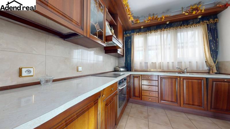 A kitchen in a 5 or more room apartment with wooden cabinets and light curtains.