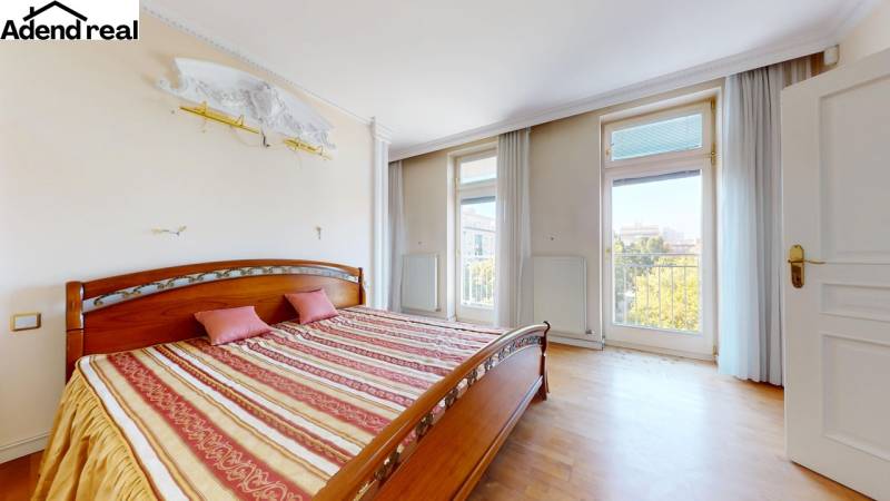 A bedroom with a bed, wooden decor flooring, and large windows in a 5 or more room apartment.