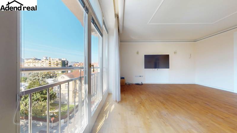 Wide windows, wooden decor flooring, TV on the wall, city view.