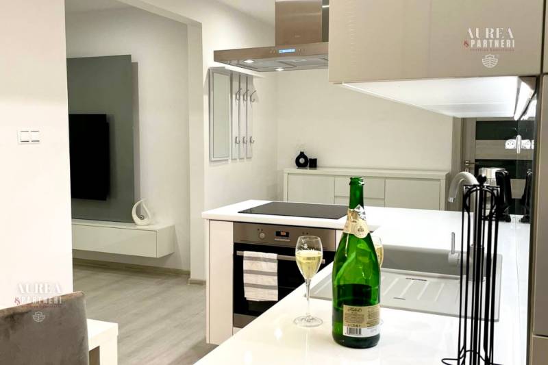 A stylish kitchen with an island, a cooktop, and a glass of wine in a two-room apartment.