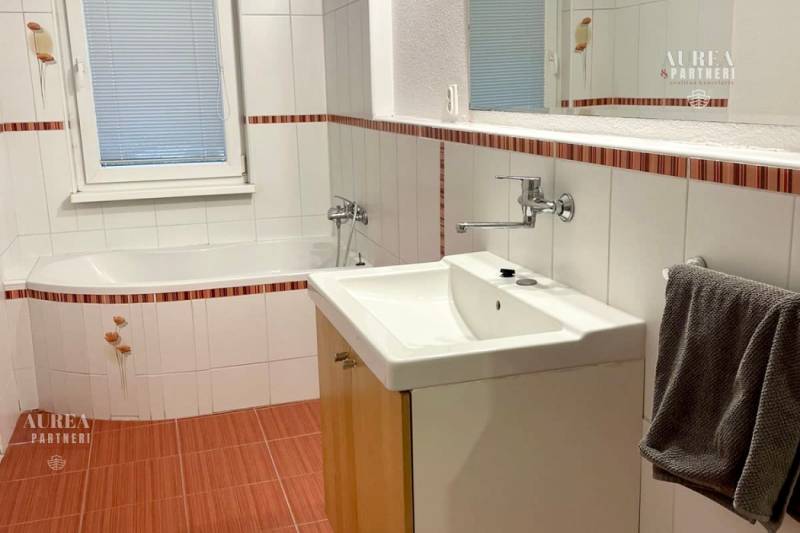 Bathroom with a bathtub, sink, and mirror in a 2-room apartment. White tiles with a decor.