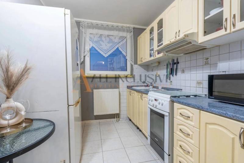 A kitchen in a 3-room apartment with white tiles, appliances, and a table.