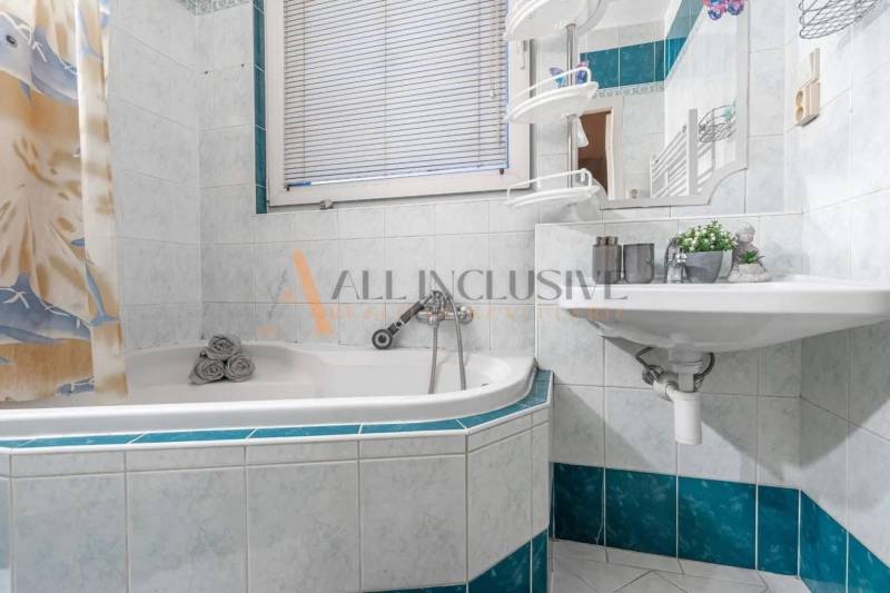 A bathroom with white and blue tiles, a corner bathtub, and a sink in a 3-room apartment.