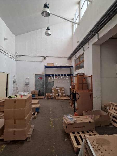 The interior of a warehouse with a high ceiling, cardboard boxes, and pallets on the floor.