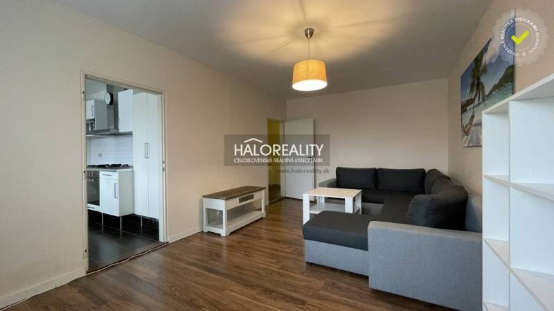 Living room in a three-room apartment with a wooden decor floor and a view into the kitchen.