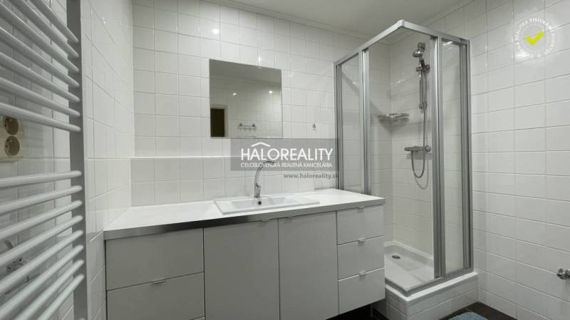 A bathroom in a 3-room apartment with white tiles, a shower corner, and a sink with a cabinet.