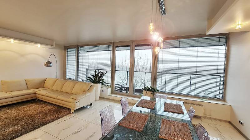 Living room of a 3-room apartment with large windows, a cream sofa, and a dining table.
