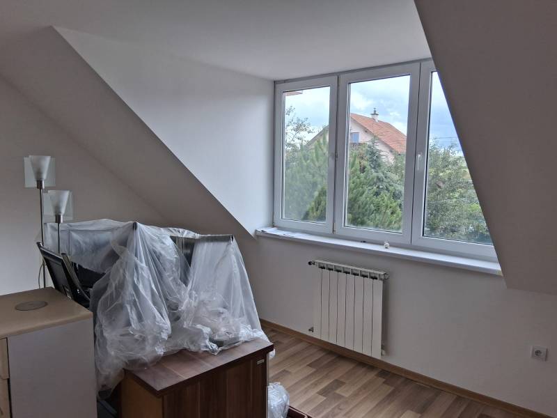 Attic room with a large window, radiator, and wooden decor flooring.